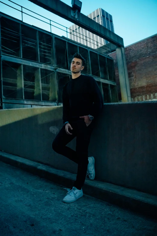 a young man leans against a wall while wearing tennis shoes