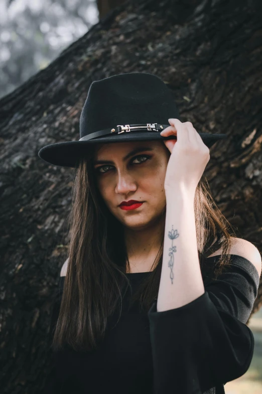 a woman wearing a hat poses in front of a tree