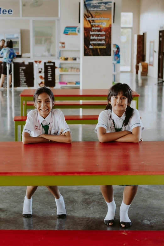 two girls sit in a cafeteria booth with their arms folded over the bench