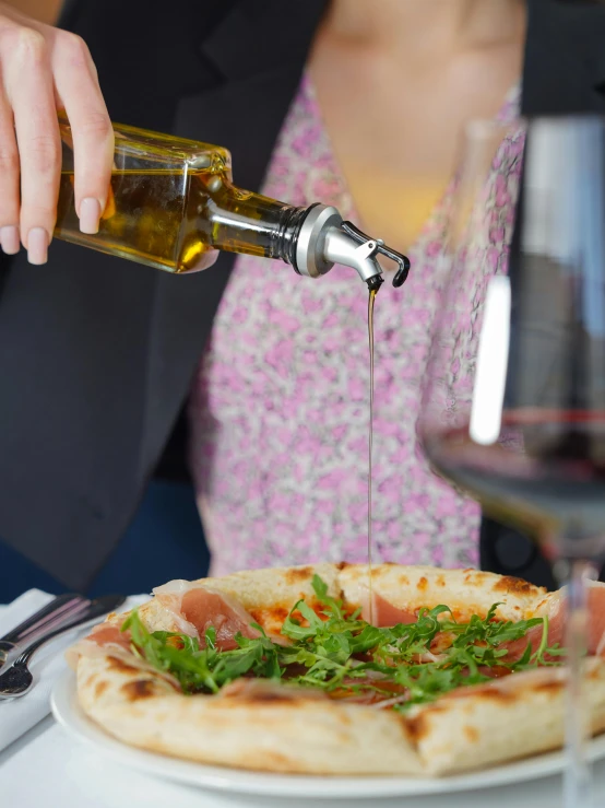 a woman is pouring a bottle of wine onto a flatbread