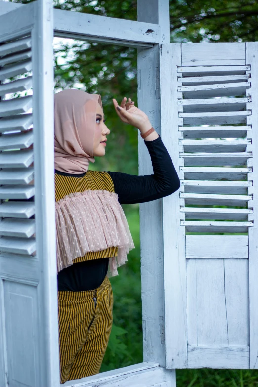 a young woman in hijab peering out an open window