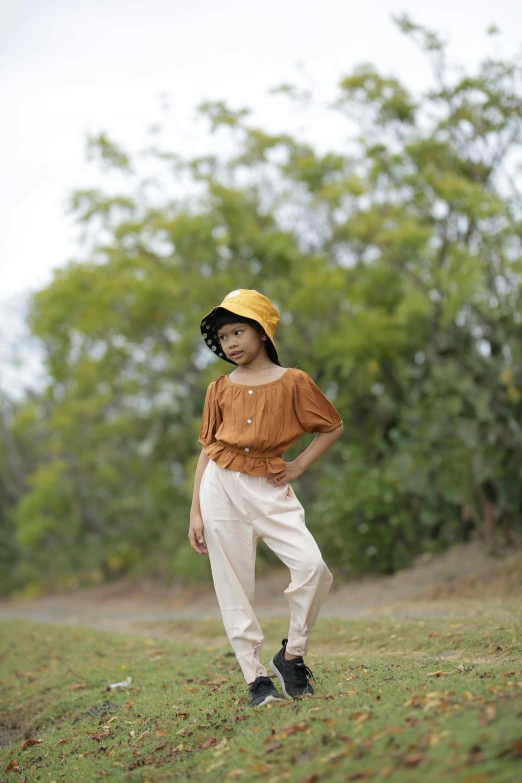 a little girl standing in the grass on a hill with trees in the background