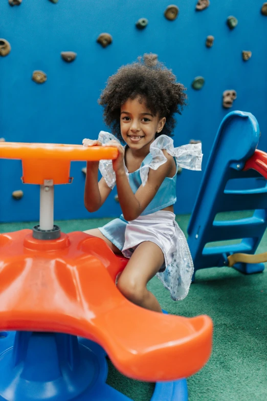 a little girl in a blue dress sitting at a toy structure