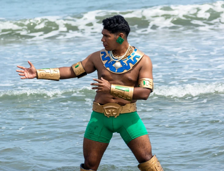 a man in green trunks and gold arm guards riding a surfboard