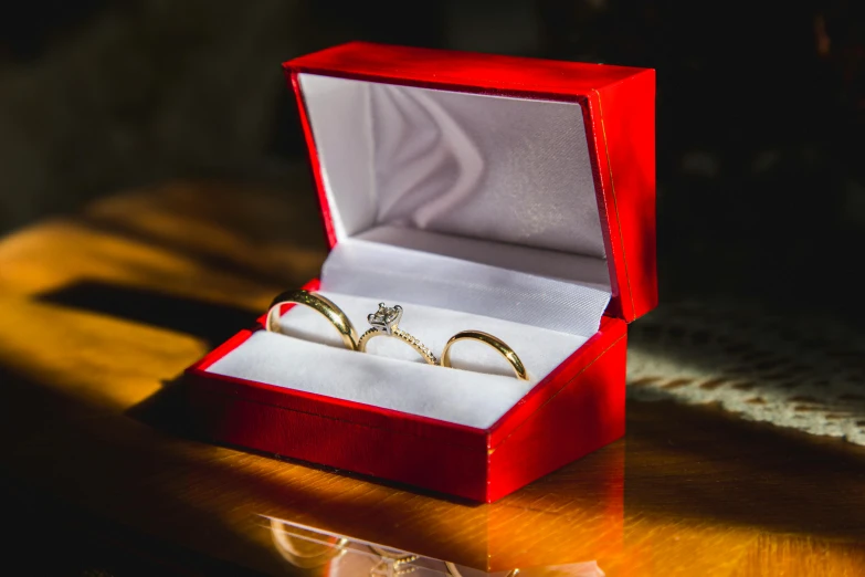 two golden engagement rings sit in an open red box