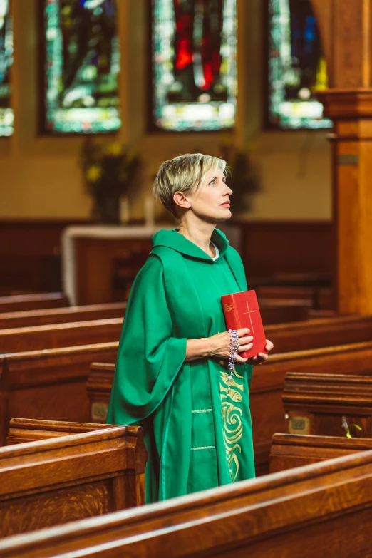 a woman stands in a pew while wearing a green robe