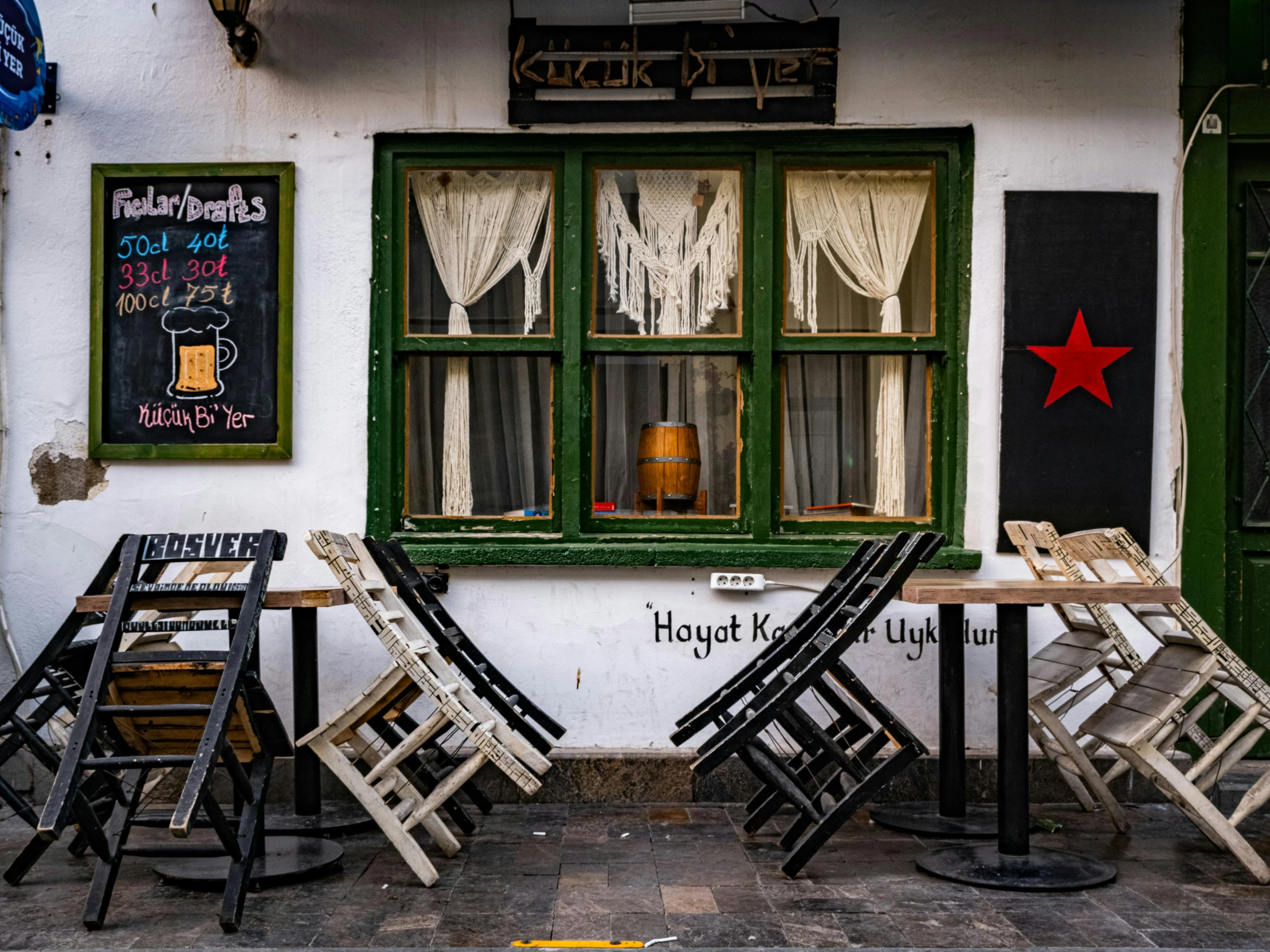 four wooden chairs outside a restaurant with two tables and three windows