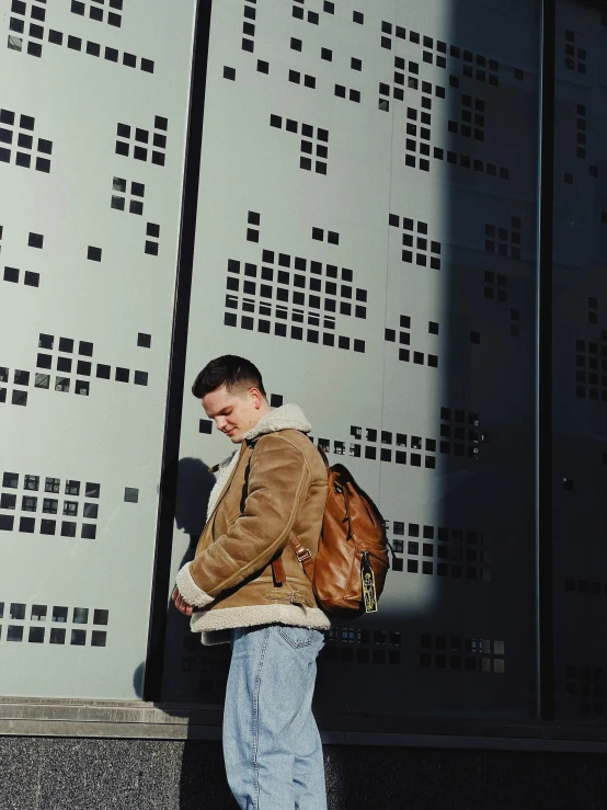 man standing near wall with leather jacket and backpack on