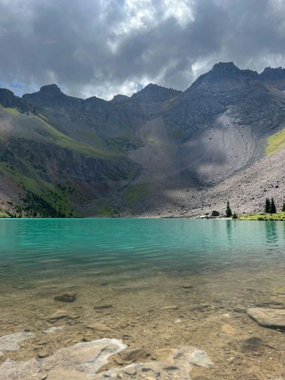 a lake that is clear and blue under a cloudy sky