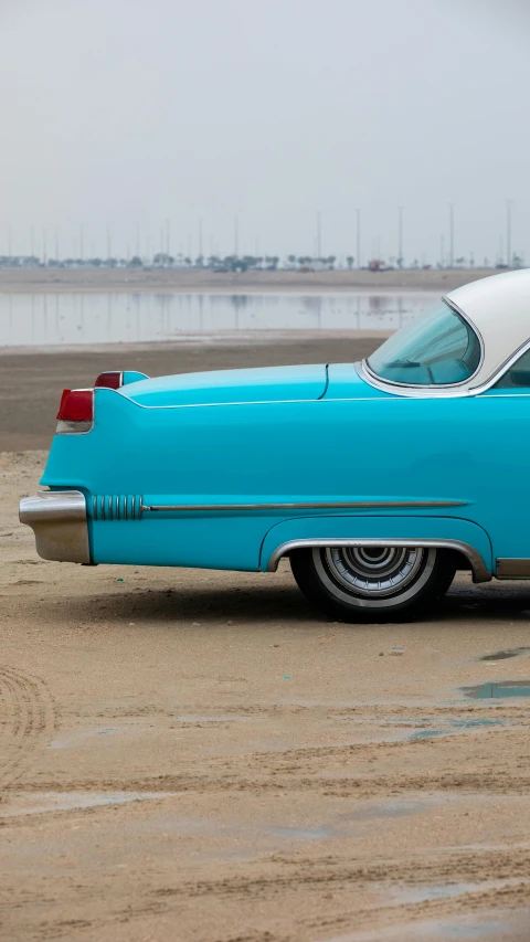 a blue classic car parked on top of a sandy beach