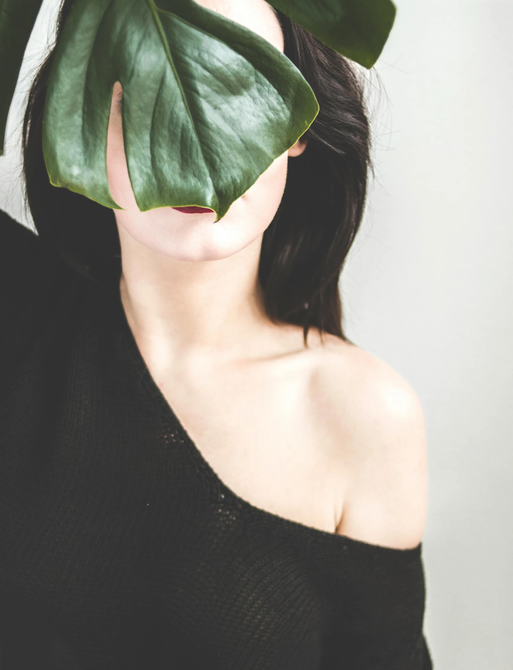 a woman with long dark hair and a green leaf covering her mouth