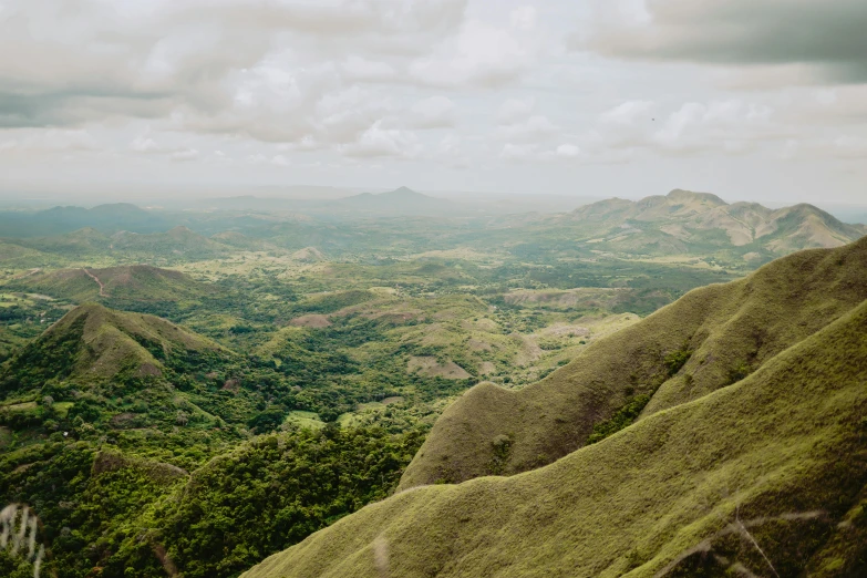 a hillside with many green hills under a cloudy sky