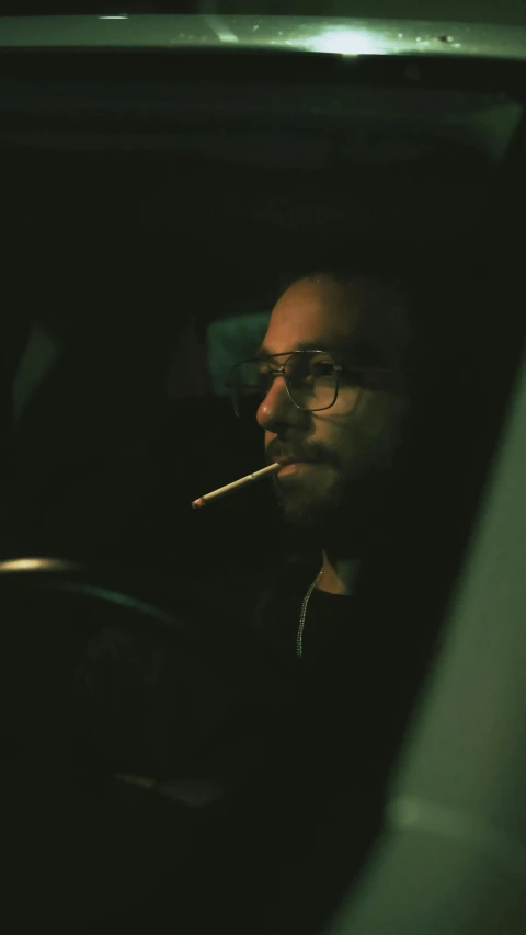 a man with glasses smokes a cigarette while in his car