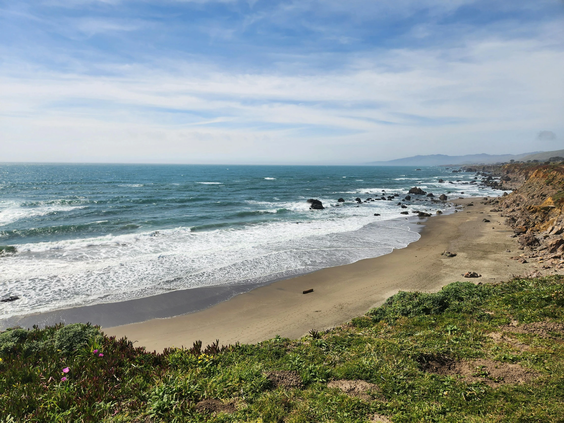 a sandy beach with ocean water on a partly cloudy day