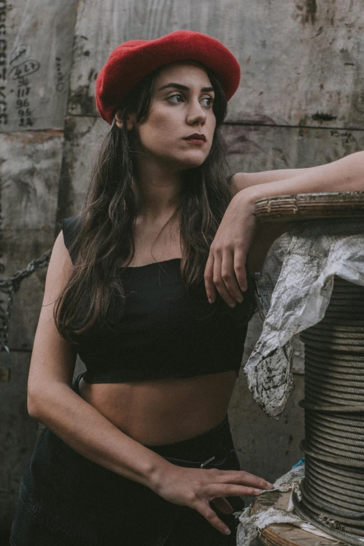 a beautiful woman leaning against a stone wall wearing a red hat