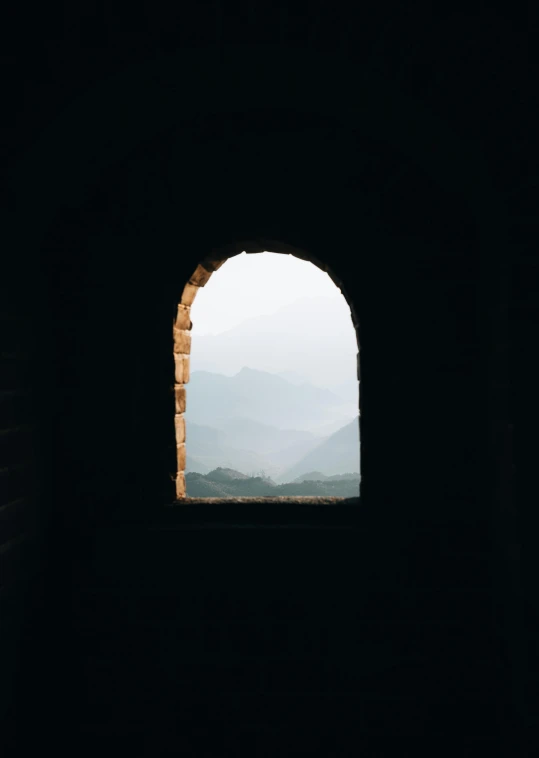 a black room with a brick archway and mountains outside