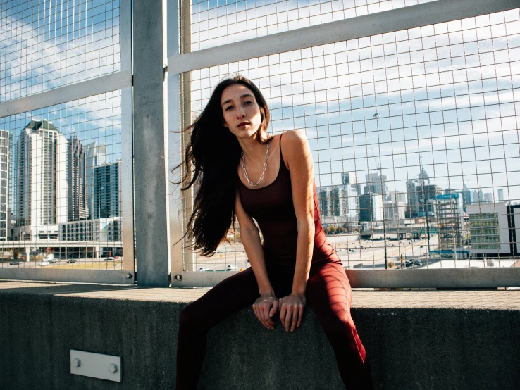 a woman wearing a brown top and dark pants is sitting outside on a wall