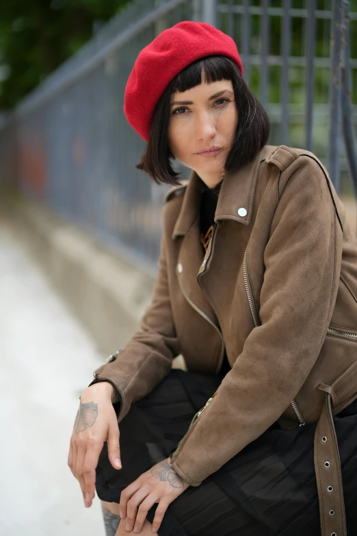 a beautiful woman with long black hair sitting on steps wearing a brown jacket and red hat