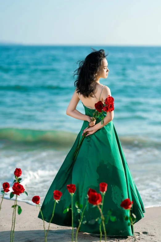 young woman in green dress standing at beach with red flowers