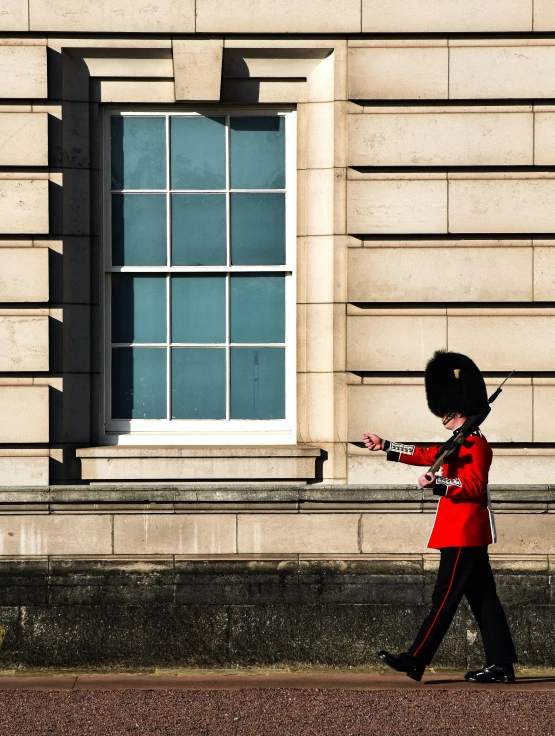 guard in red uniform walking past a big window