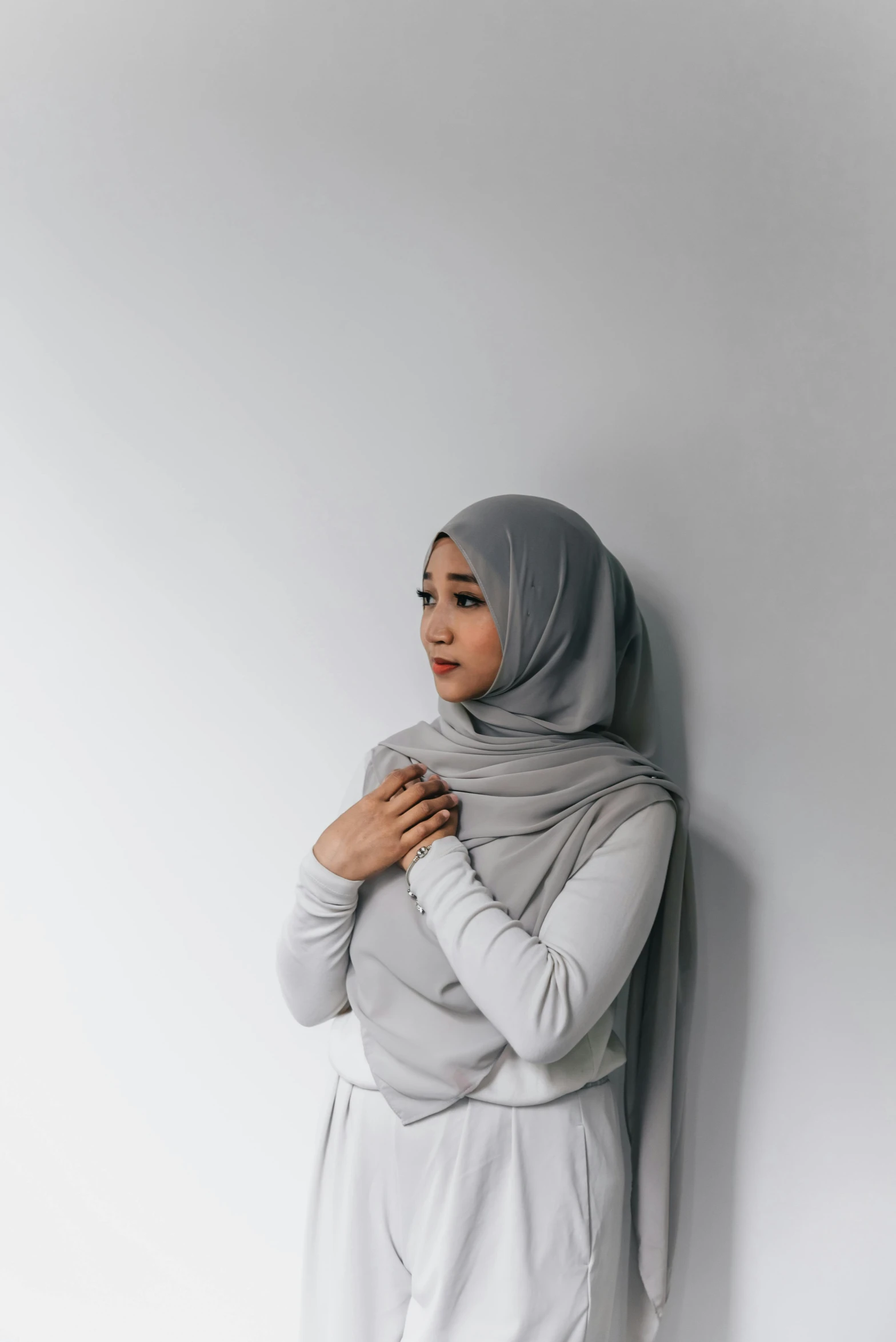 a woman in grey clothes standing against a white wall