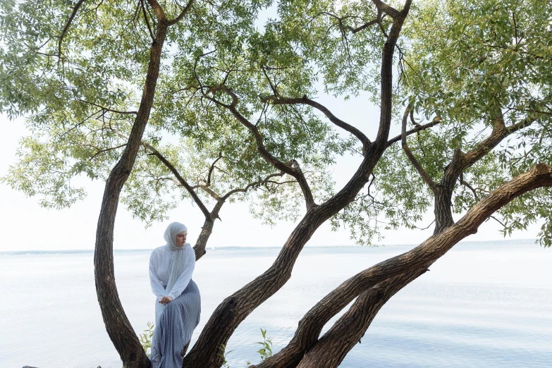 a woman standing in front of a tree near a body of water