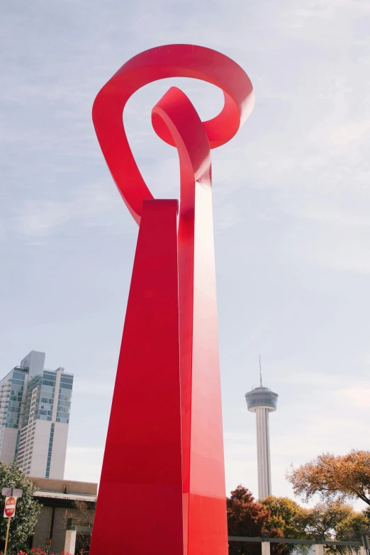 a tall red sculpture is standing in the middle of a plaza