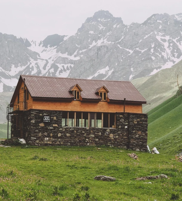 a stone house built into the side of a mountain with snow covered mountains in the background