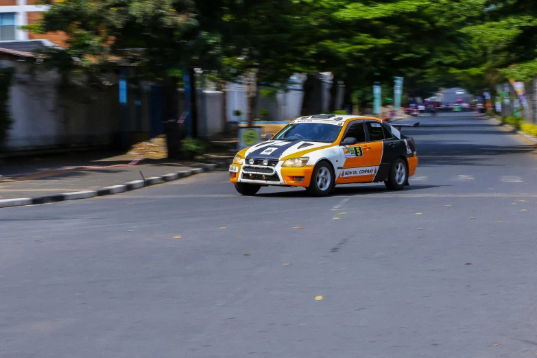 an orange car driving down the road with trees in the background