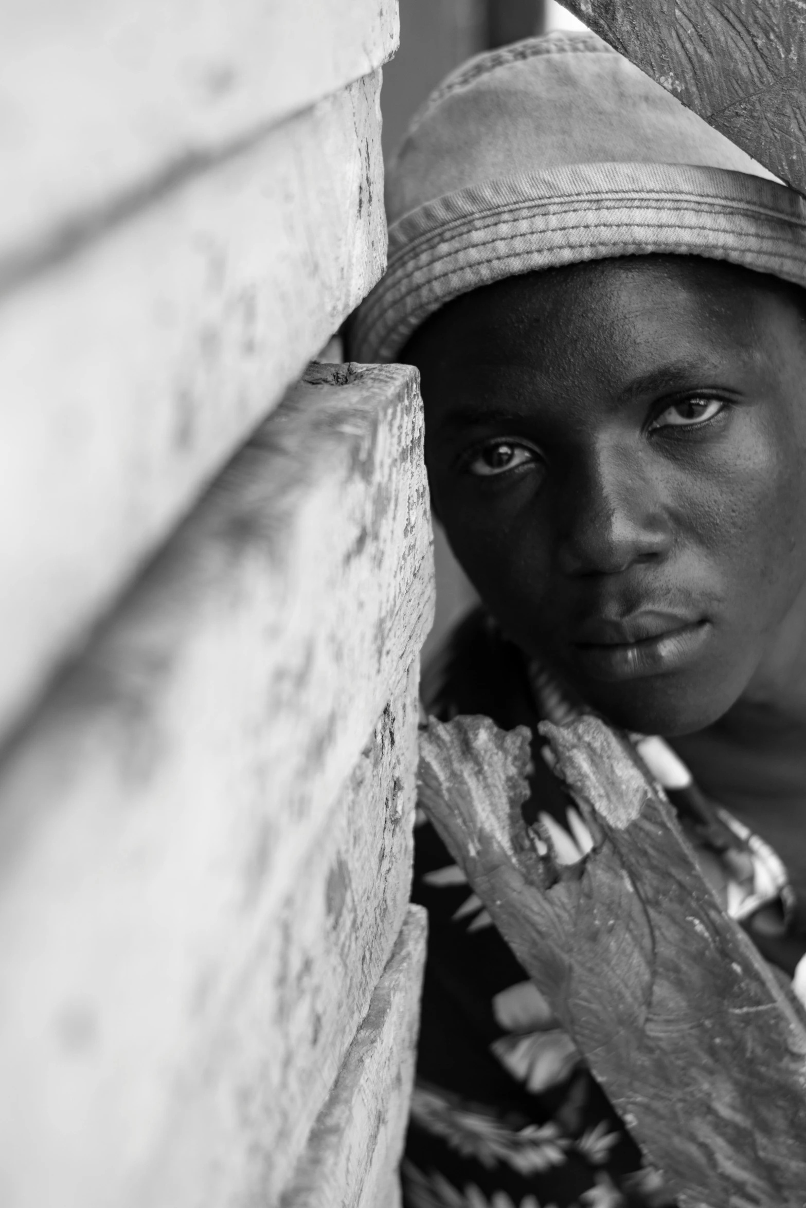 a young child stands by a wall with one eye opened