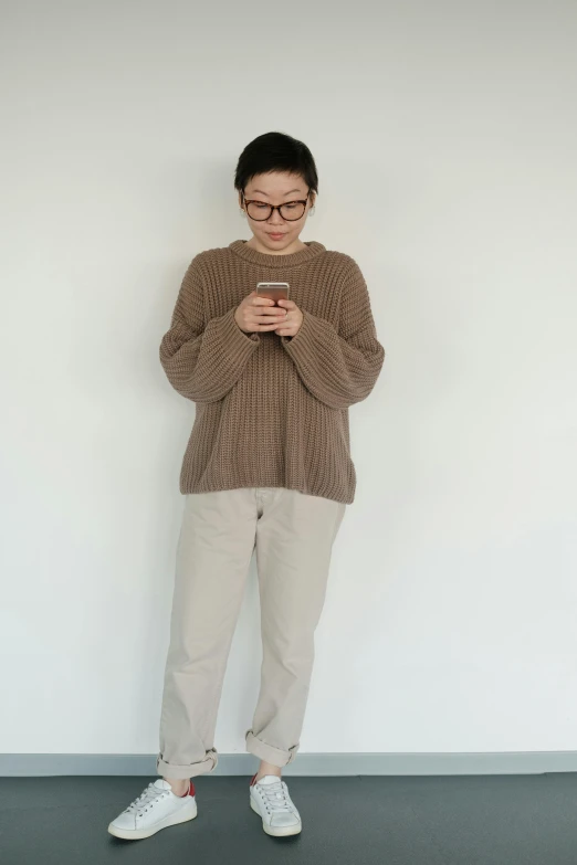 man in sweater looking at cell phone with hand on hips