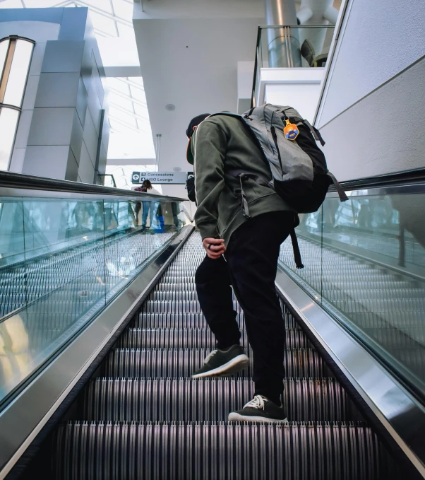 a man rides down an escalator while carrying his backpack