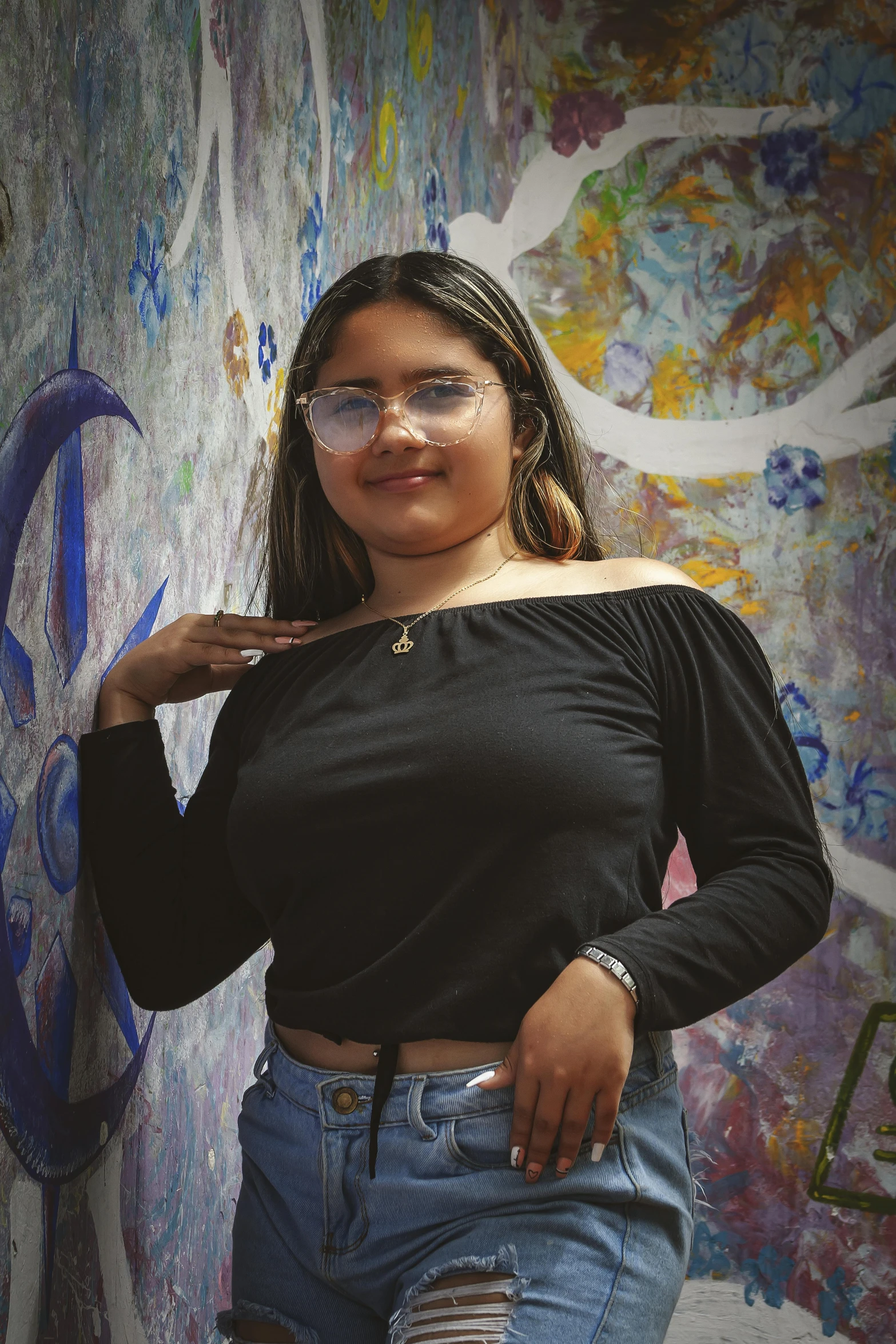 a woman wearing glasses leaning against a graffiti wall