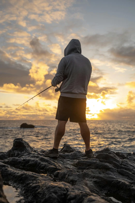 a man is fishing on rocks as the sun sets