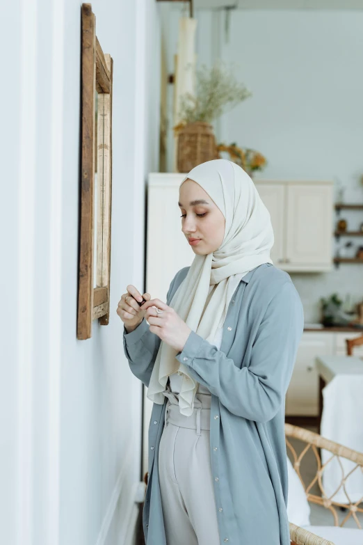 woman in hijab looking at phone by mirror in kitchen