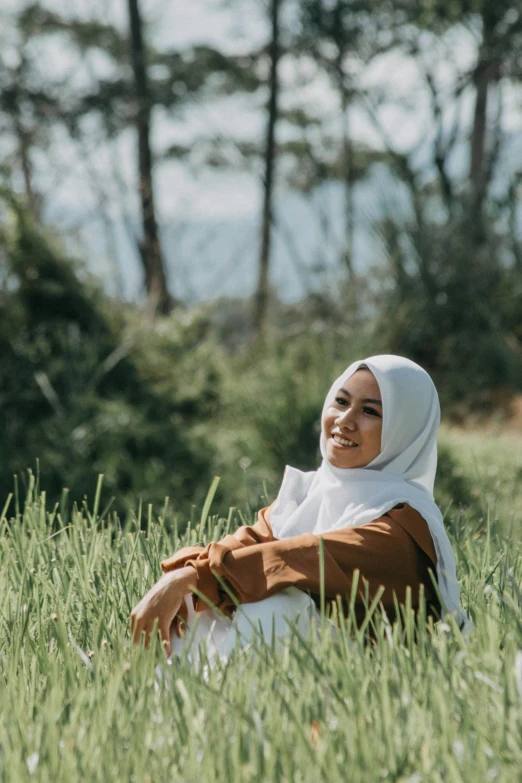 the woman in brown and white hijab is sitting in grass