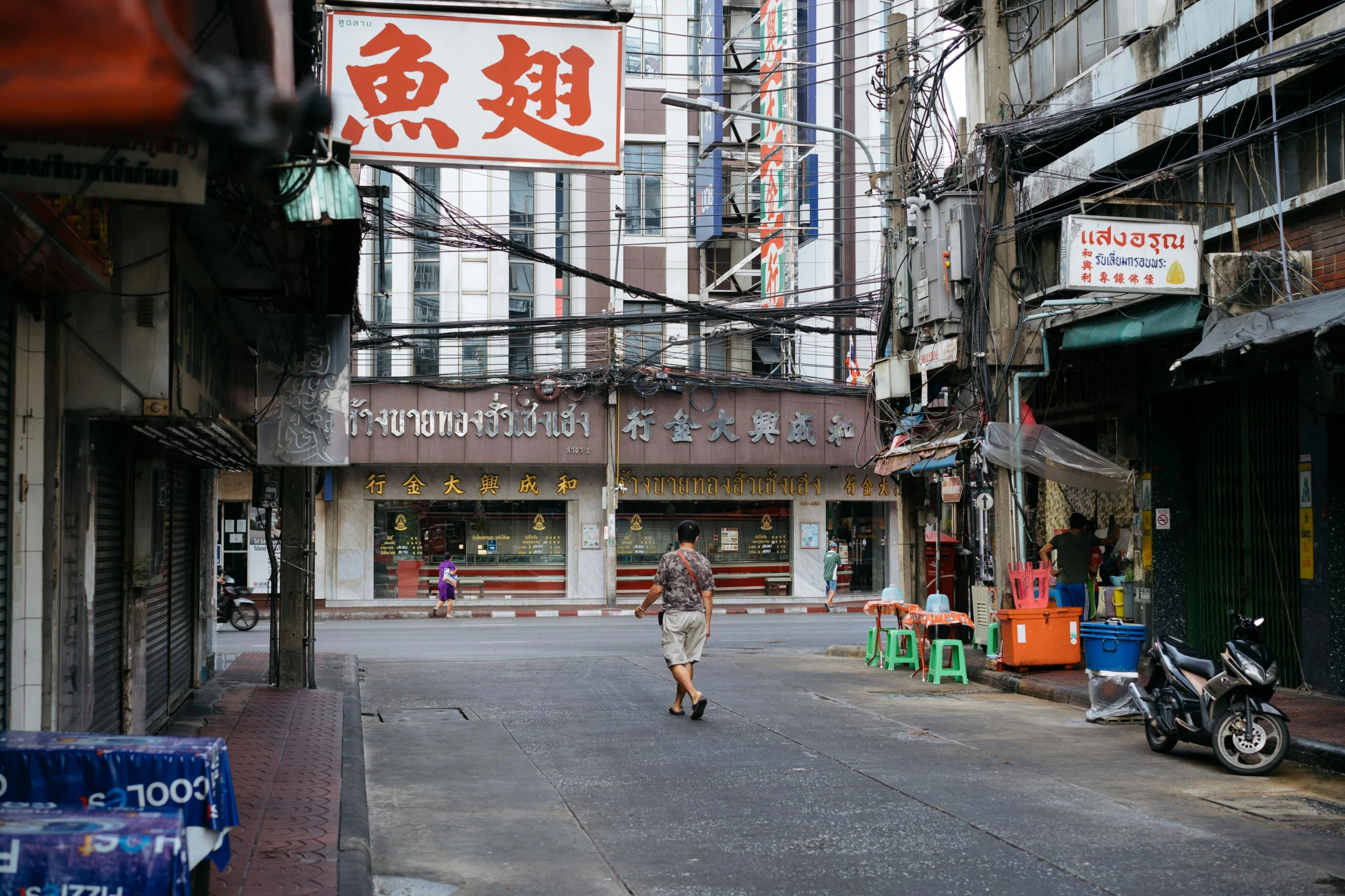 two people are walking down the street while shops sit across the road from some buildings