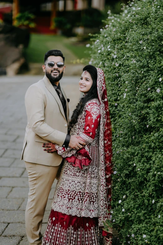 an indian bride and groom pose together near flowers in their garden