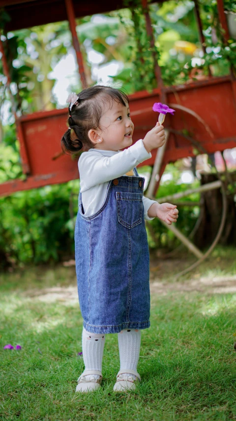a girl in a denim dress and white top with a purple flower