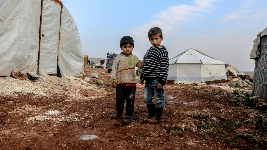 two small boys standing in an outside dirt area