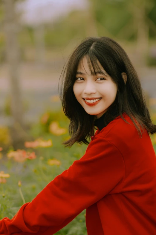 a smiling woman stands in a field with a bush and grass