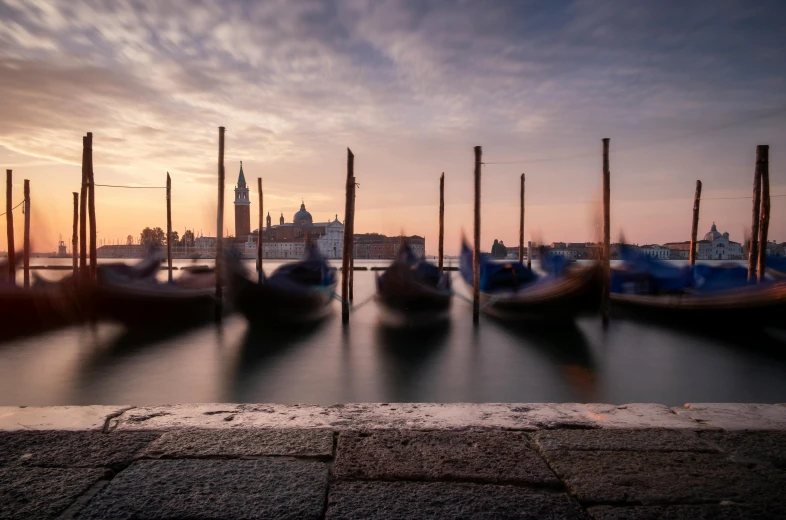 a row of gondolas parked at a pier on a sunset