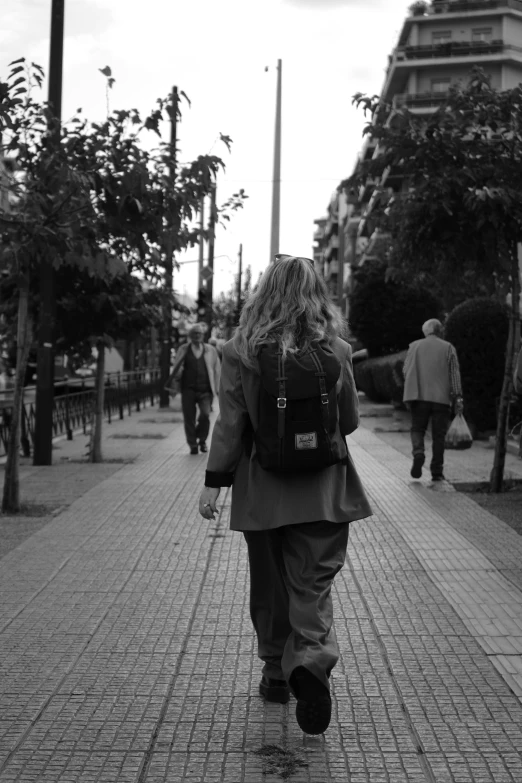 a man with long hair wearing a suit walking down a street