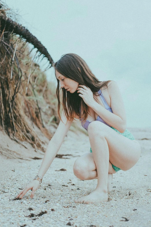 a woman in a bikini sits on the beach near palm trees