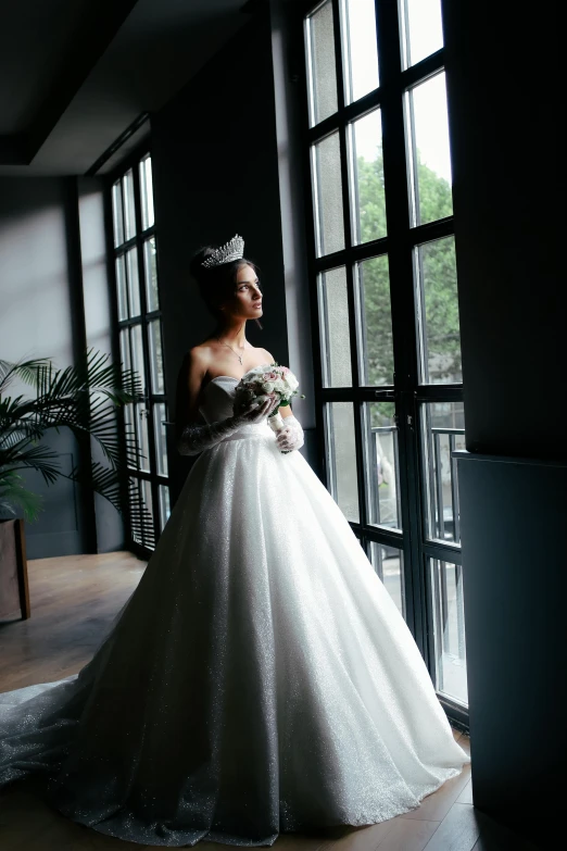 a woman standing by a window in a wedding gown