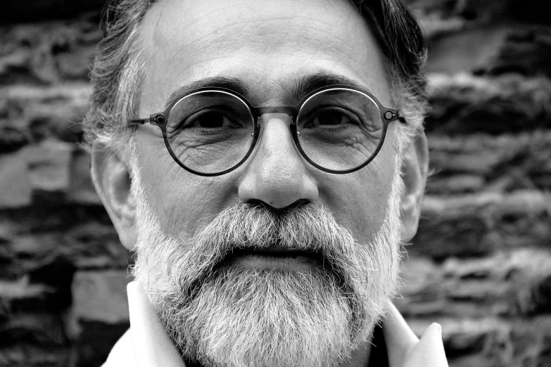 a man with glasses poses in front of a brick wall