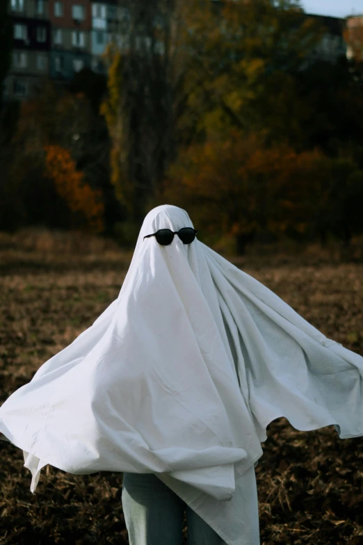 a ghost with black sunglasses hiding behind a white blanket