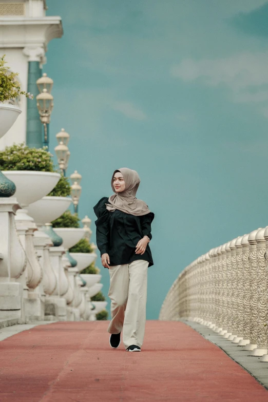 a woman in a black shirt and hijab is walking down a long red pathway