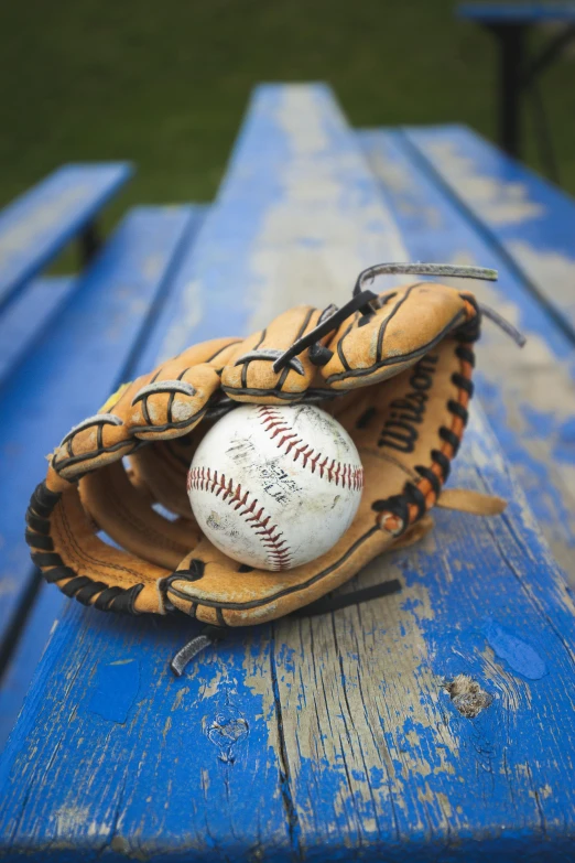 a catchers mitt, ball and glove sit on a bench