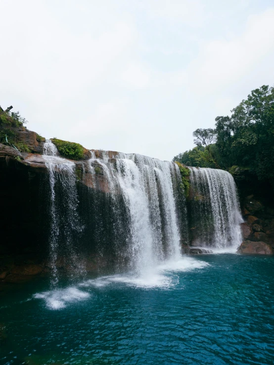 waterfall with green vegetation in foreground and blue water